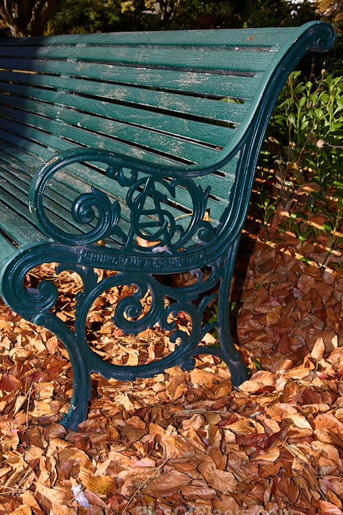 A park bench surrounded by fallen and dried autumn leaves.